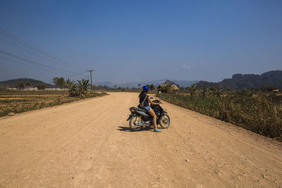 Woman riding motorcycle on dirt road against sky