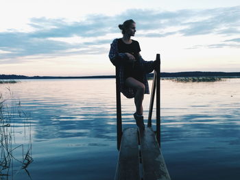 Man sitting on wooden post in lake against sky