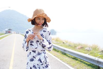 Portrait of young woman standing on road against sky