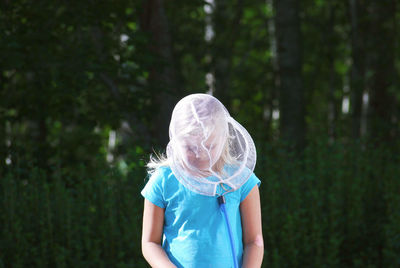 Girl wearing butterfly net on face while standing in forest