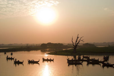 Silhouette people boating in lake against sky