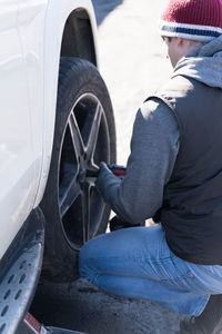 A man changes a wheel on a car, a seasonal change of rubber on a car