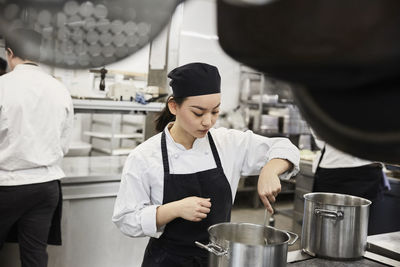 Young female chef stirring food in cooking pan at commercial kitchen