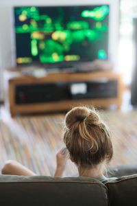 Rear view of teenage girl playing video game on sofa at home