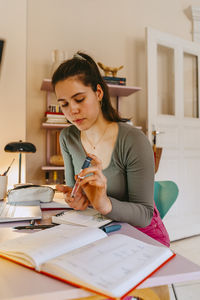 Young woman using glucometer while doing homework at table