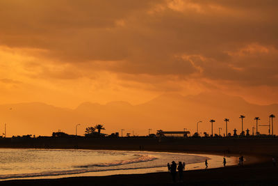 Silhouette people on beach against sky during sunset