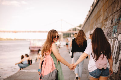 Lesbian couple holding hands while walking on promenade by river