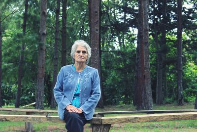 Senior woman sitting on wooden seat against trees at forest