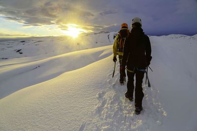 Rear view of hikers walking on snowy landscape against sky