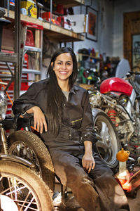 Portrait of happy female mechanic sitting in workshop