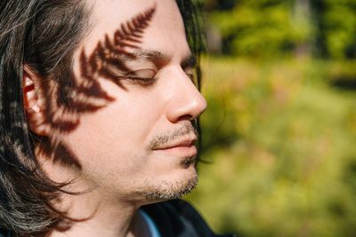 Close-up of young man with fern shadow looking away