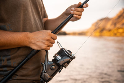 Midsection of man holding fishing rod by water