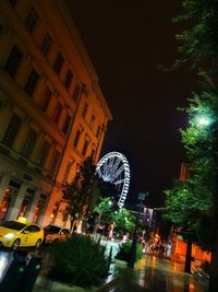 Illuminated ferris wheel by buildings in city at night