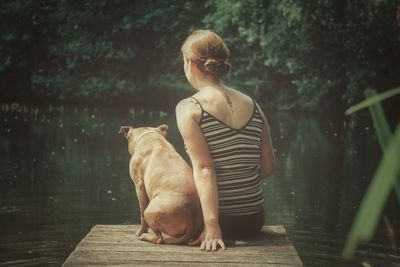 Rear view of woman with dog sitting on pier over lake