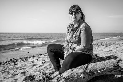 Woman sitting on rock at beach against sky