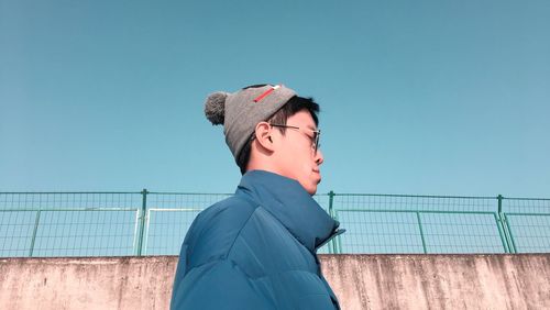 Side view of young man looking away against clear blue sky
