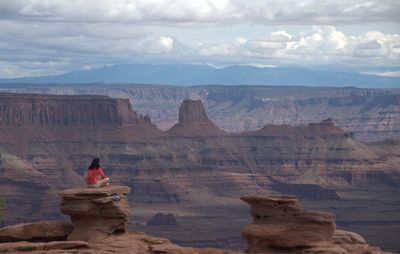 Woman sitting on rock formation against cloudy sky at dead horse point state park