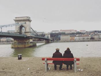 Rear view of people sitting on bridge over river