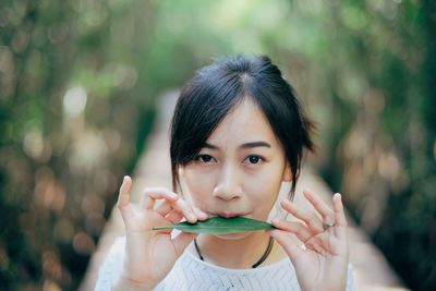 Portrait of young woman holding leaf while standing outdoors