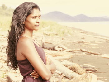 Thoughtful woman with arms crossed standing at beach