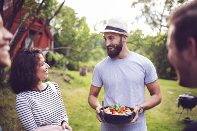 Smiling man holding food container while talking to friend in back yard