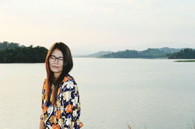 Young woman standing by lake against sky