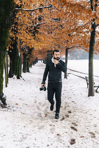 Handsome man with camera on snow covered footpath during winter