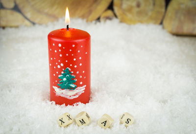 Close-up of lit candle on fake snow during christmas