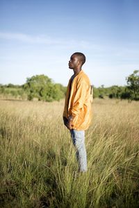 Side view of man standing on field against sky