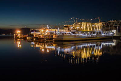 Sailboats moored in sea against illuminated city at night