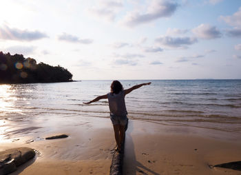 Rear view of woman with arms outstretched balancing at beach