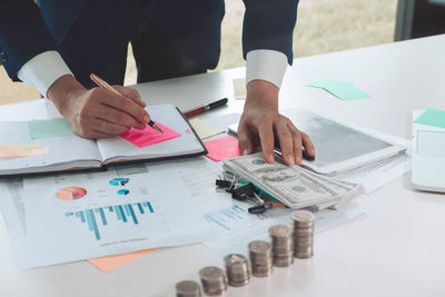 Midsection of businessman counting currency at desk while writing on diary