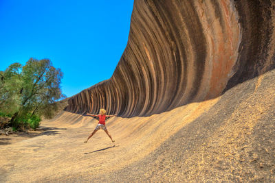 Woman with arms outstretched jumping by cliff