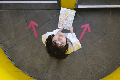 Young woman looking up holding map standing by arrow symbols