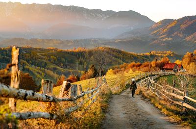Scenic view of man walking on country road against mountain and sky during autumn at sunset