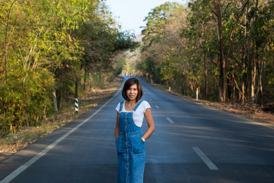 Portrait of woman standing on road amidst trees