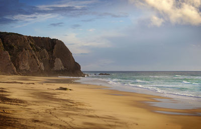Scenic view of sandy beach in sunset light with rocky cliff on the background