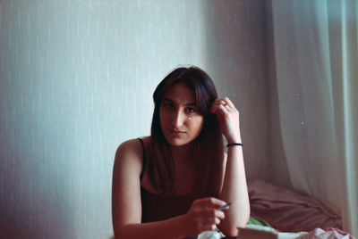 Portrait of young woman sitting against wall at home