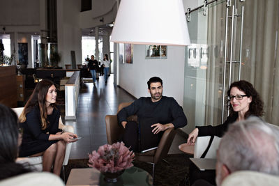 Business people discussing while sitting on armchairs in office lobby