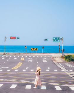 Woman crossing road by sea against clear sky