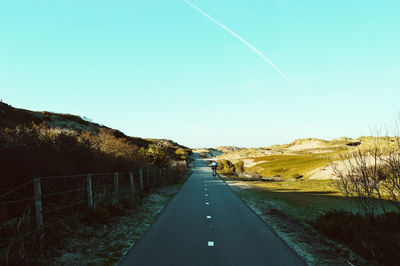 Country road amidst fields against clear sky