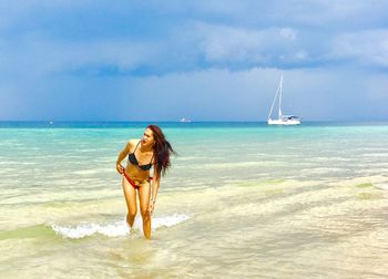 Young woman in bikini on beach against sky