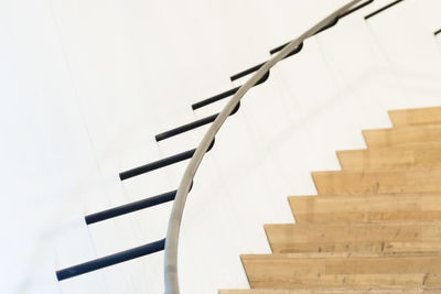 Metallic railing over wooden staircase by white wall