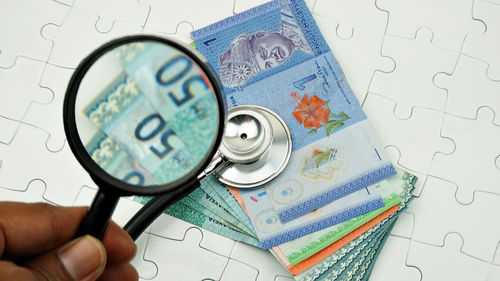 Close-up high angle view of hand holding magnifying glass over stethoscope and money on puzzle