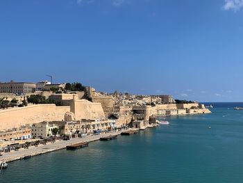 Buildings by sea against clear blue sky