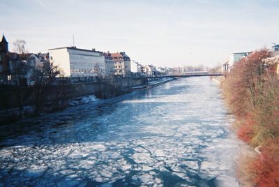 Frozen river in city against sky