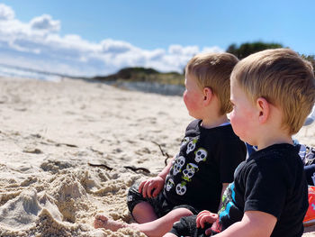 Baby boys sitting at beach against sky