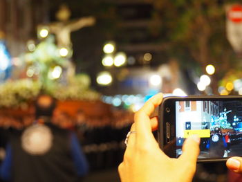 Cropped image of hand photographing illuminated mobile phone at night