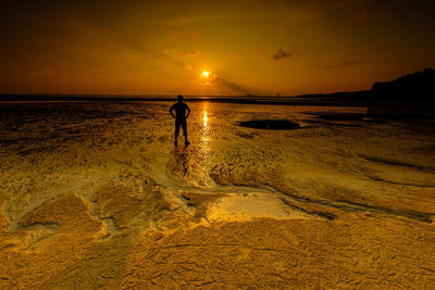 Silhouette man standing on beach against sky during sunset