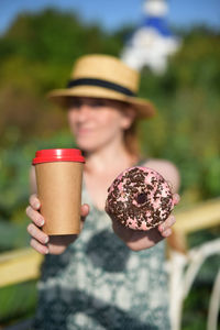 Woman holding donut and disposable cup in sunny day